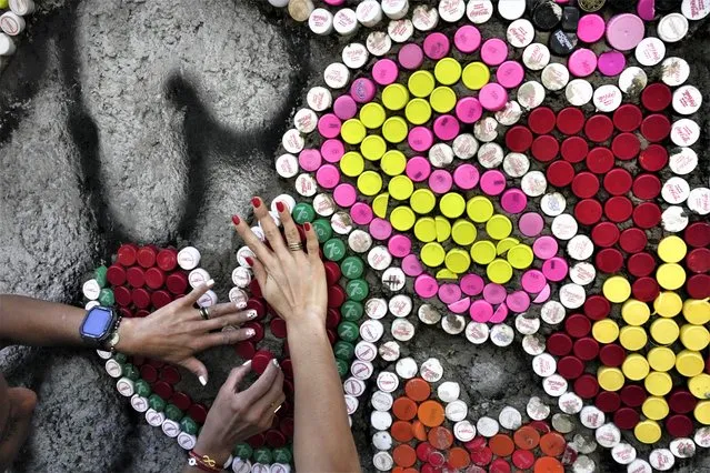 Women attach bottle caps to a wall in Los Caobos public park in Caracas, Venezuela, Wednesday, December 21, 2022. A Venezuelan artist organized a project with recycled bottle caps titled “Wall of Love”, in order to raise awareness of those who have been affected by climate change in Venezuela and the world. (Photo by Matias Delacroix/AP Photo)