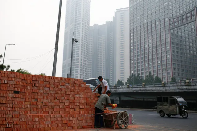 Workers load a cart with bricks at a construction site in Beijing, China, September 16, 2016. (Photo by Thomas Peter/Reuters)