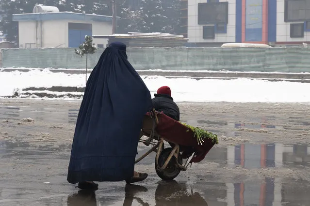A burqa-clad woman pushes a wheelbarrow loeaded with vegetables and a child during snow fall in Kabul on January 11, 2023. (Photo by Wakil Kohsar/AFP Photo)