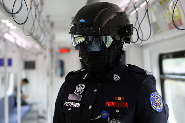 An auxiliary police officer wearing “Smart Helmet”, a portable thermoscanner that can measure the temperature of passengers at a distance, patrols inside a commuter train, amid the coronavirus disease (COVID-19) outbreak in Kuala Lumpur, Malaysia on October 14, 2020. (Photo by Lim Huey Teng/Reuters)