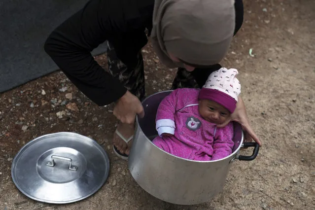 A Syrian mother carries her baby girl in a cooking pot at Ritsona refugee camp north of Athens, Wednesday, October 12, 2016. About 600 people, mostly families with small children, live in tents in the camp, which officials say will soon be replaced by prefabricated homes. (Photo by Petros Giannakouris/AP Photo)