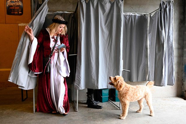 A voter in a medieval costume faces a dog as she comes out of the polling booth  in the communal workshops where the polling station has been set up during the town's medieval festival, which takes place over the weekend in Rodemack, north eastern France on June 30, 2024. A divided France is voting in high-stakes parliamentary elections that could see the anti-immigrant and eurosceptic party of Marine Le Pen sweep to power in a historic first. The candidates formally ended their frantic campaigns at midnight June 28, with political activity banned until the first round of voting. (Photo by Jean-Christophe Verhaegen/AFP Photo)