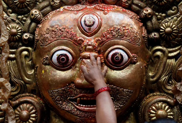 A hand of a devotee is pictured as she sprinkles rice grains while offering prayer on the mask of Bhairab, which is kept on the chariot of Rato Machhindranath, during the chariot festival in Lalitpur, Nepal April 27, 2018. Rato Machhindranath is known as the god of rain and both Hindus and Buddhists worship Machhindranath for good rainfall to prevent drought during the rice harvest season. (Photo by Navesh Chitrakar/Reuters)
