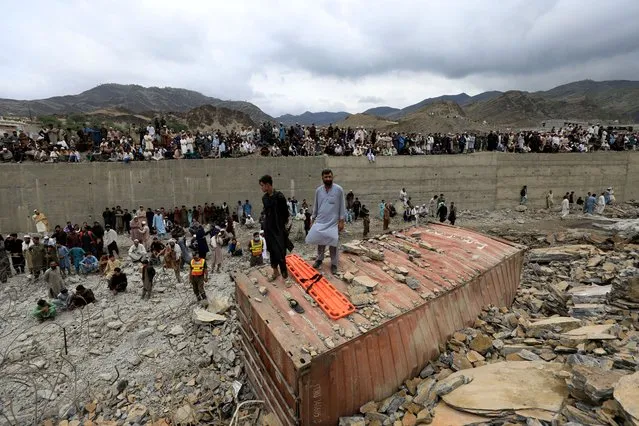 Rescue members and onlookers stand around a damaged supply vehicle after a landslide close to the Torkham border in Pakistan on April 18, 2023. (Photo by Fayaz Aziz/Reuters)
