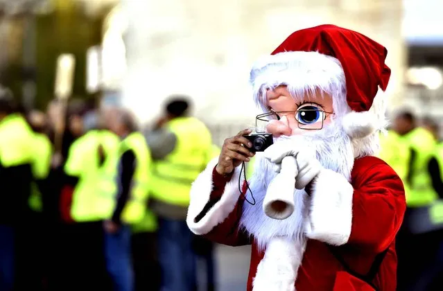 A man posing for tourist in a Santa Claus disguise takes a picture at the Puerta del Sol square in the centre of Madrid on November 26, 2015. (Photo by Gerard Julien/AFP Photo)