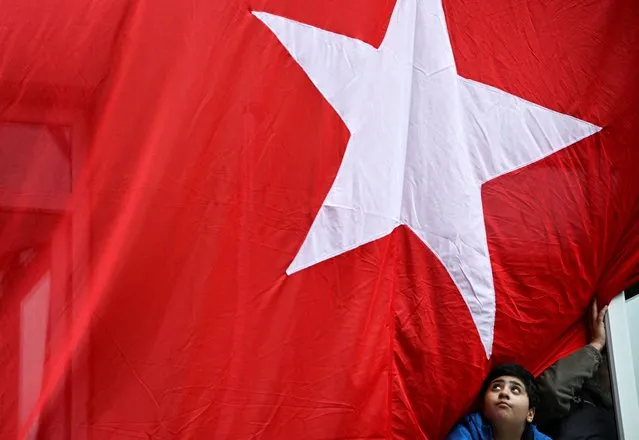 A boy looks out a window of a building where a Turkish flag hangs ahead of the presidential and parliamentary elections, in Istanbul, Turkey on May 12, 2023. (Photo by Dylan Martinez/Reuters)