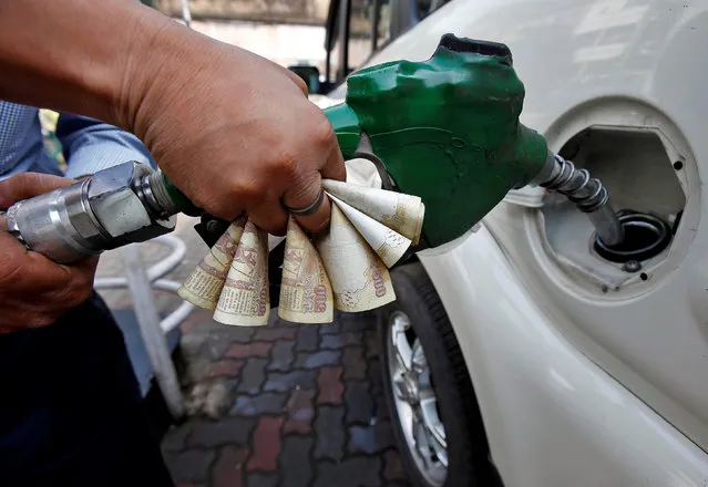 A worker fills diesel in a car as he holds 500 Indian rupee banknotes at a fuel station in Kolkata, India, November 9, 2016. (Photo by Rupak De Chowdhuri/Reuters)