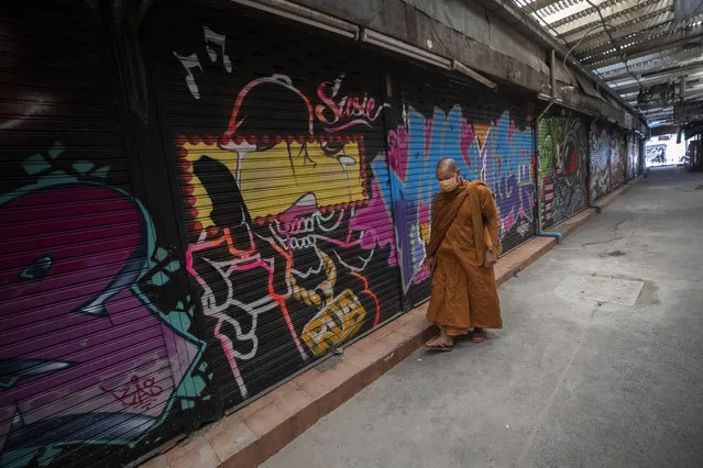 Thai Buddhist monk wearing a face mask to help curb the spread of the coronavirus walks pass closed shops in Khao San road, a popular hangout for Thais and tourists in Bangkok, Thailand Wednesday, February 3, 2021. Amid fears of new variants of the virus, new restrictions on movement have hit just as people start to look ahead to what is usually a busy time of year for travel. (Photo by Sakchai Lalit/AP Photo)