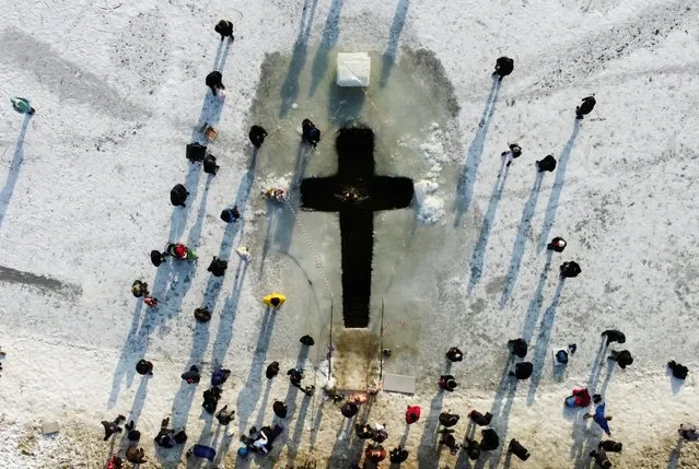 People gather around a cross-shaped ice hole during celebrations of the Orthodox Christian feast of Epiphany in Kyiv, Ukraine on January 19, 2021. (Photo by Valentyn Ogirenko/Reuters)