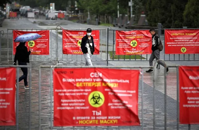 People walk past banners informing of preventive measures against the coronavirus disease (COVID-19) in Almaty, Kazakhstan on May 20, 2021. (Photo by Pavel Mikheyev/Reuters)
