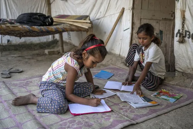 Garima, 10, right, and her sister Arima, 7, left, study outside their restored home on the flood plain of Yamuna River after coming from school in New Delhi, India, Friday, September 29, 2023. (Photo by Altaf Qadri/AP Photo)