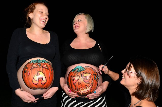 Two expectant mothers Anna Glendining,25 (left) and Gemma Wilkinson, 30 (right) celebrate Halloween by having pumpkins painted on their bumps. They were painted by artist Jane Pryde (far right) from Allendale, Northumberland, on October 30, 2013. (Photo by Owen Humphreys/PA Wire)