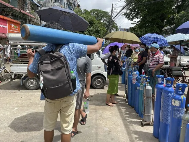 A man carries an oxygen tank while others line up with their oxygen tanks outside an oxygen refill station in Pazundaung township in Yangon, Myanmar, Sunday, July 11, 2021. Myanmar is facing a rapid rise in COVID-19 patients and a shortage of oxygen supplies just as the country is consumed by a bitter and violent political struggle since the military seized power in February. (Photo by AP Photo/Stringer)