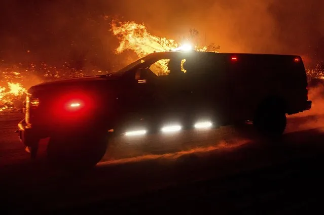 Firefighters drive along Highway 395 south of Janesville in Lassen County, Calif., as the Dixie Fire jumps the roadway on Monday, August 16, 2021. Critical fire weather throughout the region threatens to spread multiple wildfires burning in Northern California. (Photo by Noah Berger/AP Photo)