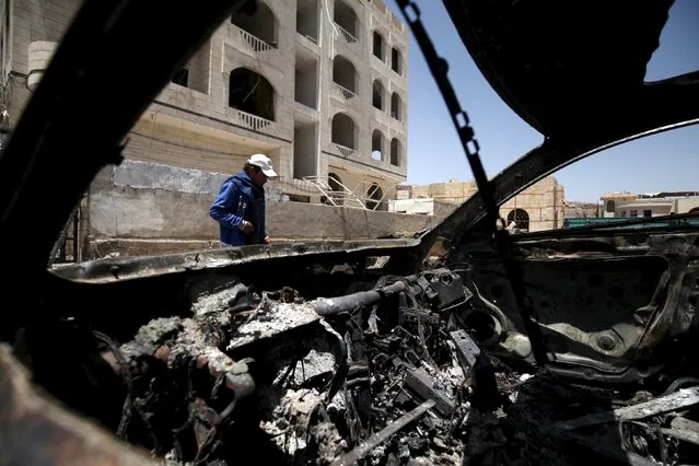 A man walks in front of a damaged car, after an April 20 air strike that hit a nearby army weapons depot, in Sanaa April 21, 2015. (Photo by Mohamed al-Sayaghi/Reuters)