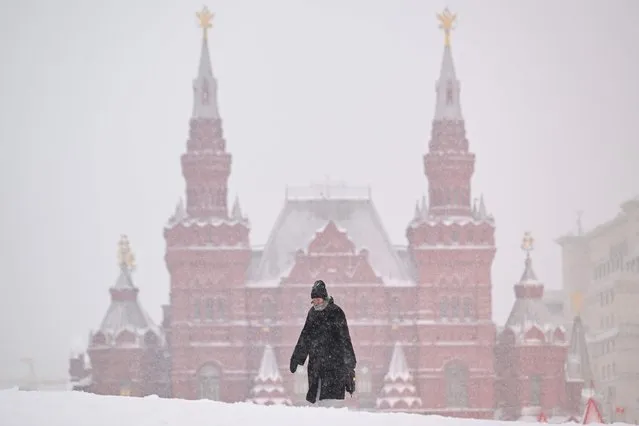 A woman walks on Red Square, with the State Historical Museum seen in distance, during a heavy snowfall in Moscow on February 7, 2024. (Photo by Natalia Kolesnikova/AFP Photo)