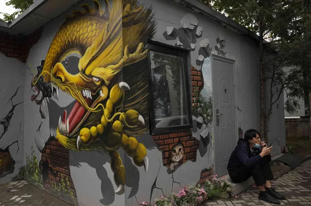 A man lowers his mask for a smoke break near a mural depicting a dragon in Beijing, China, Tuesday, October 5, 2021. (Photo by Ng Han Guan/AP Photo)