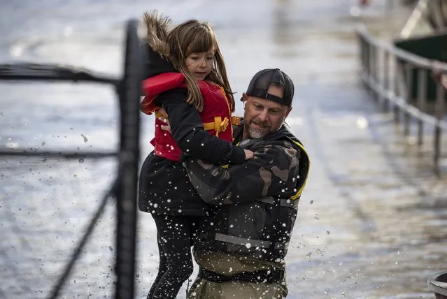 A volunteer carries a young girl to high ground after using a boat to rescue a woman and children who were stranded by high water due to flooding in Abbotsford, British Columbia on Tuesday, November 16, 2021. Officials in a small city near the Canada border are calling the damage devastating after a storm that dumped rain for days caused flooding and mudslides. City officials in Sumas, Washington said Tuesday that hundreds of people had been evacuated and estimated that 75% of homes had water damage. Just over the border, residents in about 1,100 rural homes in Abbotsford were told to evacuate as waterways started to rise quickly. (Photo by Darryl Dyck/The Canadian Press via AP Photo)
