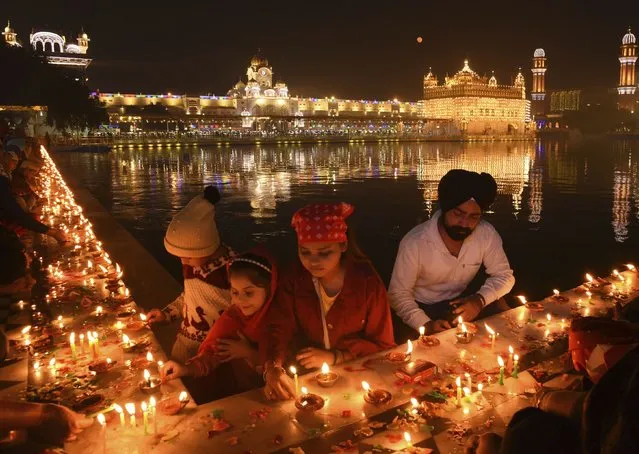 Sikh devotees Light candles at the illuminated Golden Temple on the occasion of the birth anniversary of Guru Nanak, the first Sikh Guru and the founder of Sikhism, in Amritsar, India, Friday, November 19, 2021. (Photo by Prabhjot Gill/AP Photo)