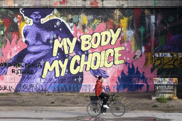 A person goes by bike along the Danube Canal during the lockdown in Vienna, Austria, Tuesday, December 7, 2021. A graffiti on the wall in the back says “my body, my choice”. (Photo by Lisa Leutner/AP Photo)