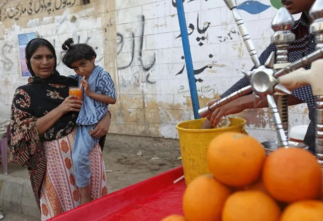 A woman holds a glass orange juice for her daughter to drink next to a cart along a road in Karachi, Pakistan, April 22, 2016. (Photo by Akhtar Soomro/Reuters)
