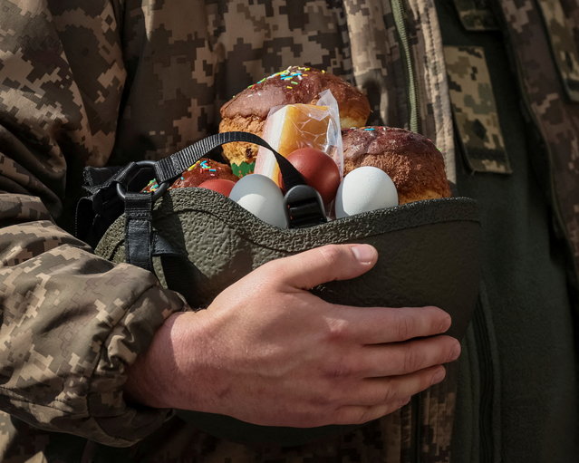 A Ukrainian serviceman holds an Easter cake in a helmet during a ceremony to bless Easter cakes and eggs outside the Volodymysky Cathedral, amid Russia's invasion of Ukraine, in Kyiv, Ukraine on April 24, 2022. (Photo by Gleb Garanich/Reuters)