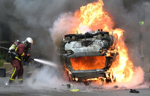 A firefighter extinguishes a burning car at the end of a commemoration march for a teenage driver shot dead by a policeman, in the Parisian suburb of Nanterre, on June 29, 2023. Violent protests broke out in France in the early hours of June 29, 2023, as anger grows over the police killing of a teenager, with security forces arresting 150 people in the chaos that saw balaclava-clad protesters burning cars and setting off fireworks. Nahel M., 17, was shot in the chest at point-blank range in Nanterre in the morning of June 27, 2023, in an incident that has reignited debate in France about police tactics long criticised by rights groups over the treatment of people in low-income suburbs, particularly ethnic minorities. (Photo by Alain Jocard/AFP Photo)