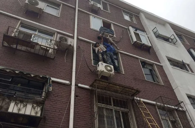 Liu Xinjun (L) and Jia Xiaoyu (R) hold a woman who fell out a window at her home in Tianjin, June 20, 2014. Liu and Jia held up an elderly who fell out her window and was stuck on a rack of an air-conditioner for five minutes, as another man Yang Ming held on to the woman with a rope from inside the room while waiting for firefighters to rescue. (Photo by Reuters/China Daily)