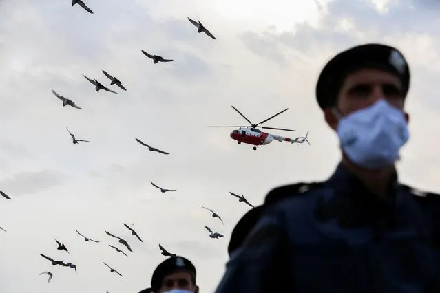 A police helicopter is seen flying over police officials wearing face masks during their march-past celebrate Police Day, commemorating the fifty-seventh anniversary of the Libyan Police Day, in Tripoli, Libya, October 9, 2021. (Photo by Hazem Ahmed/Reuters)