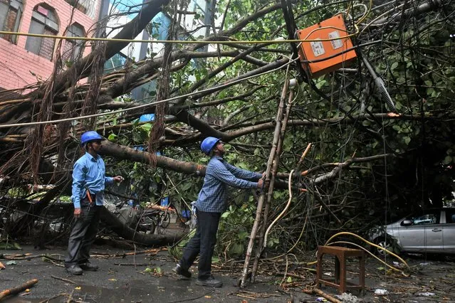 Men try to repair a damaged pole next to a fallen tree after heavy wind and rain in New Delhi, India on May 30, 2022. (Photo by Shashi Shekhar Kashyap/Reuters)