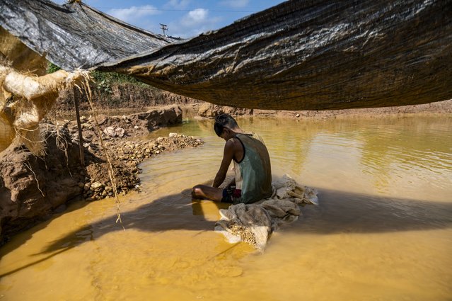 A young Venezuelan miner uses a wooden container to strain and separate mercury from the mud used to adhere gold found in an open pit mine, which will then be sold in El Callao, Bolivar State, Venezuela, on August 27, 2023. In the town of El Callao, extracting gold from soil starts off as a kid's game, but soon becomes a full-time job that human rights activists says amounts to child exploitation. (Photo by Magda Gibelli/AFP Photo)