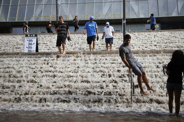 Dominic Aguilera slides down a hand rail into a parking structure outside Pauley Pavilion sporting arena as water flows down stairs from a broken thirty inch water main that was gushing water onto Sunset Boulevard near the UCLA campus in the Westwood section of Los Angeles July 29, 2014. The geyser from the 100-year old water main flooded parts of the campus and stranded motorists on surrounding streets. (Photo by Danny Moloshok/Reuters)