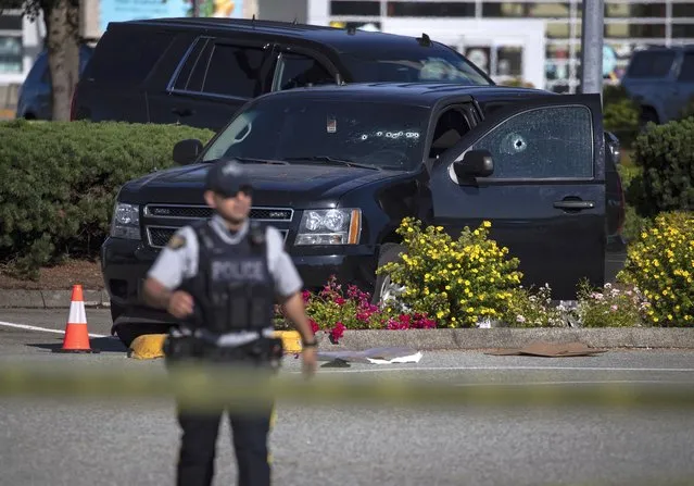 A police officer standing near a windshield and passenger window of an RCMP vehicle with bullet holes at the scene of a shooting in Langley, British Columbia, Monday, July 25, 2022. Canadian police reported multiple shootings of homeless people Monday in a Vancouver suburb and said a suspect was in custody. (Photo by Darryl Dyck/The Canadian Press via AP Photo)