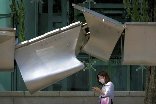 A woman wearing a face mask walks by an art installation depicting two colliding aircraft carriers on display outside a mall in Beijing, Sunday, August 7, 2022. Taiwan said Saturday that China's military drills appear to simulate an attack on the self-ruled island, after multiple Chinese warships and aircraft crossed the median line of the Taiwan Strait following U.S. House Speaker Nancy Pelosi's visit to Taipei that infuriated Beijing. (Photo by Andy Wong/AP Photo)