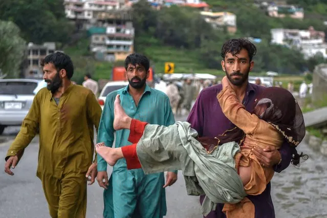 A man (R) carries his sick daughter along a road damaged by flood waters following heavy monsoon rains in Madian area in Pakistan's northern Swat Valley on August 27, 2022. (Photo by Abdul Majeed/AFP Photo)