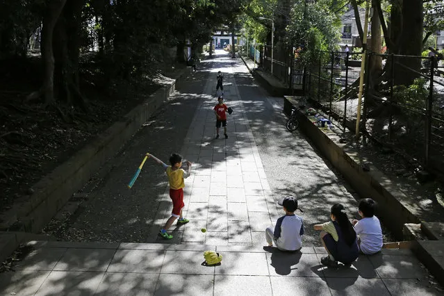 In this April 19, 2020, file photo, children, some wearing protective masks to prevent the spread of the coronavirus, play baseball on a walkway to Shibuya Hikawa-Jijja shinto shrine in Tokyo. Under Japan's coronavirus state of emergency, people have been asked to stay home. Many are not. Some still have to commute to their jobs despite risks of infection, while others are dining out, picnicking in parks and crowding into grocery stores with scant regard for social distancing. (Photo by Kiichiro Sato/AP Photo/File)