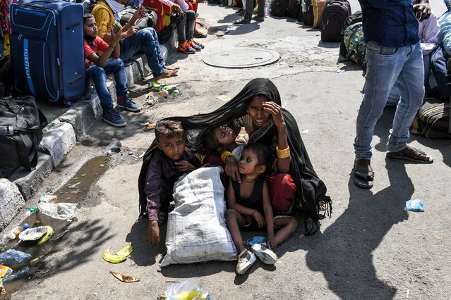 A woman covers her children with a shawl to protect them from the sun as she waits with other migrant workers and families to get registered for a train going to their native places after the goverment eased a nationwide lockdown imposed as a preventive measure against the COVID-19 coronavirus, in New Delhi on May 20, 2020. (Photo by Prakash Singh/AFP Photo)