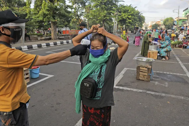 A city official takes the temperature reading of a vendor as others sit on a marked positions to maintain physical distancing in an attempt to curb the spread of the new coronavirus outbreak at a traditional market in Surabaya, East Java, Indonesia, Wednesday, June 3, 2020. (Photo by Trisnadi/AP Photo)