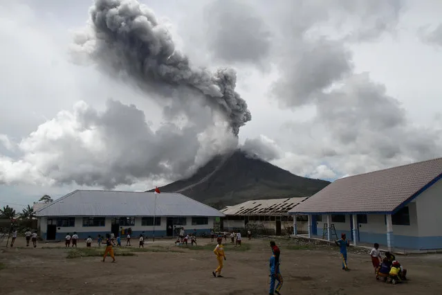 Primary school children play outside their classroom as Mount Sinabung, active since 2010, erupts in the distance in Naman Teran Village, Karo, North Sumatra, Indonesia on November 13, 2017. (Photo by Albert Damanik/Reuters)