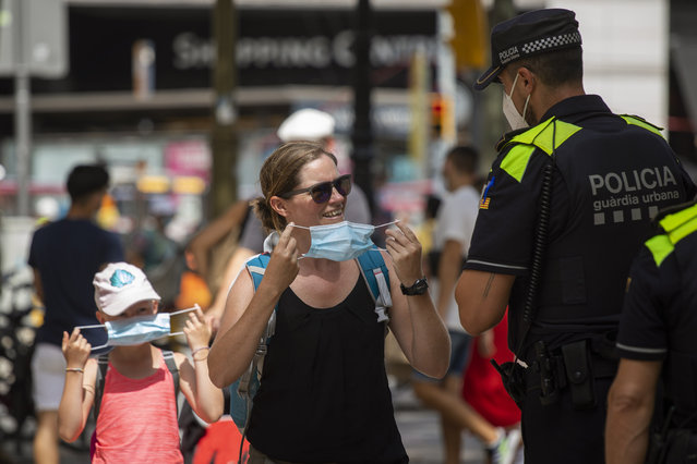 Catalonian police officers ask at a woman to wear a face mask, in Las Ramblas of Barcelona, Spain, Thursday, July 9, 2020. Authorities in northeast Spain will start fining individuals who do not wear face masks 100 euros ($113) as of Thursday when their use becomes obligatory in Barcelona and the surrounding Catalonia region. (Photo by Emilio Morenatti/AP Photo)