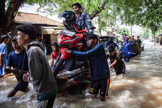 People move a scooter on a cart through a flooded area after some rivers overflowed following heavy rain in Bekasi, a suburb of Jakarta, on March 5, 2025. (Photo by Aditya Irawan/AFP Photo)