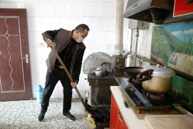 A man shovels coal into a tray next to an oven he uses to heat his home in his kitchen in the village of Heqiaoxiang outside of Baoding, Hebei province, China, December 5, 2017. (Photo by Thomas Peter/Reuters)