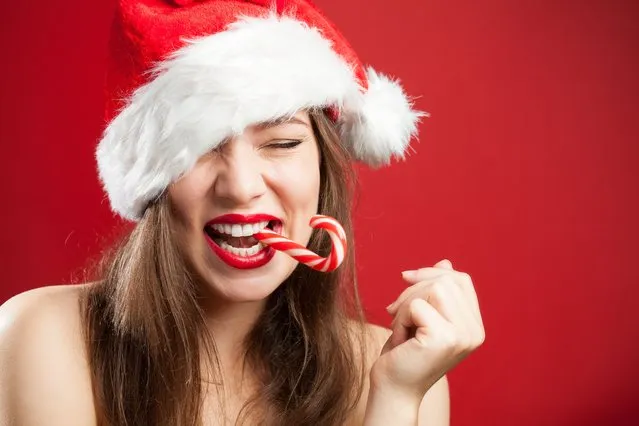 Cute sеxy caucasian brunette young woman dressed as Mrs. Santa Claus, smiling with joy, biting a candy cane with eyes closed, Christmas or New Years Eve 2022 concept. (Photo by Cryptographer/Rex Features/Shutterstock)