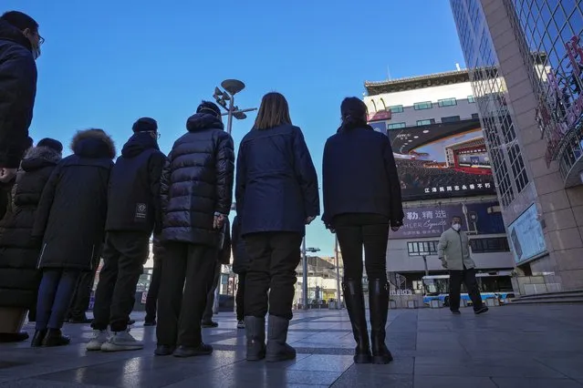 A worker walks by a group of people stand watch at an outdoor screen showing a live broadcast of the memorial service for late former Chinese President Jiang Zemin, at the Wangfujing shopping street in Beijing, Tuesday, December 6, 2022. (Photo by Andy Wong/AP Photo)