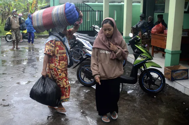 People carry their belongings as they arrive at a school turned into temporary shelter for those affected by the eruption of Mount Semeru, in Lumajang, East Java, Indonesia, Sunday, December 4, 2022. (Photo by Hendra Permana/AP Photo)