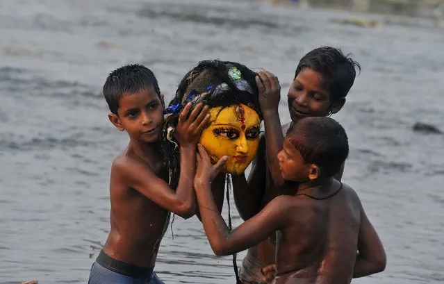 Indian boys carry the head of a clay idol of goddess Durga after it was immersed by Hindu devotees in the Mahananda river in Siliguri on Ocotber 22, 2015, at the end of the Durga Puja festival. Durga Puja commemorates the slaying of demon king Mahishasur by goddess Durga, marking the triumph of good over evil. (Photo by Diptendu Dutta/AFP Photo)