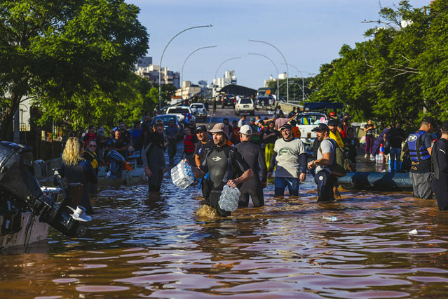 This handout photo released by the Porto Alegre City Hall (PMPA) shows a group of volunteers on a flooded street of Porto Alegre, Rio Grande do Sul State, Brazil, on May 6, 2024. From top to bottom, rescuers scour buildings in Porto Alegre for inhabitants stuck in apartments or on rooftops as unprecedented flooding killed at least 78 people in the southern state, with dozens missing and some 115,000 forced to leave their homes. (Photo by Giulian Serafim/PMPA via AFP Photo)