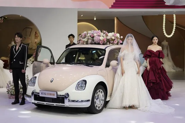 Models in wedding gowns showcase the Ora Funky Cat EV car model by Great Wall Motor during the Auto Shanghai 2023 at the National Exhibition and Convention Center in Shanghai, China, Tuesday, April 18, 2023. (Photo by Ng Han Guan/AP Photo)