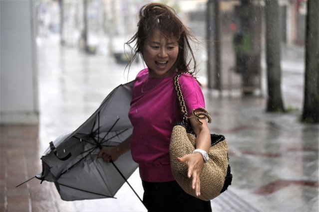 A pedestrian reacts as she caught a gust of wind while walking down the famed “Kokusai-dori” street, a tourist spot, in Naha in the main Okinawa island, southern Japan, Thursday, June 1, 2023, as a tropical storm was approaching. (Photo by Hiro Komae/AP Photo)