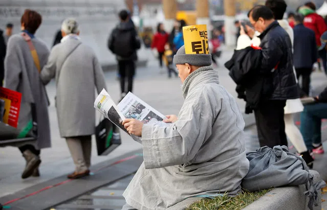 A Buddhist monk, seen with a sign denouncing South Korean President Park Geun-hye on his cap, reads a newspaper at a protest calling Park to step down, in Seoul, South Korea, November 19, 2016. (Photo by Kim Hong-Ji/Reuters)